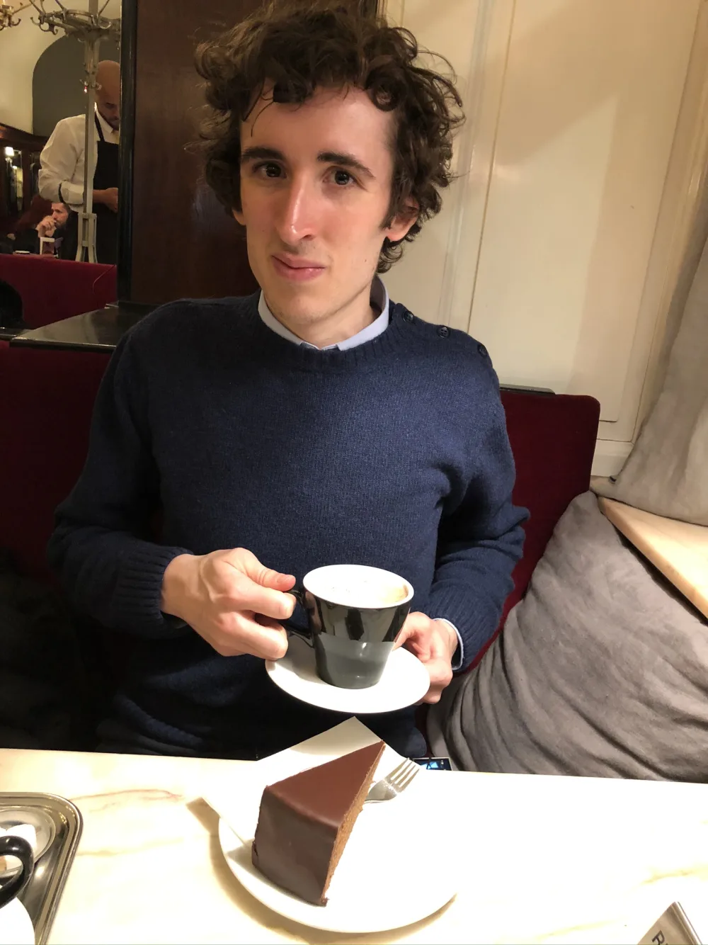 Pierre-Henry Soria tenant une tasse de café devant une part de chocolat